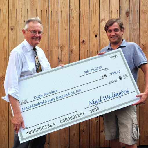 Two men holding a large check in front of a wooden fence